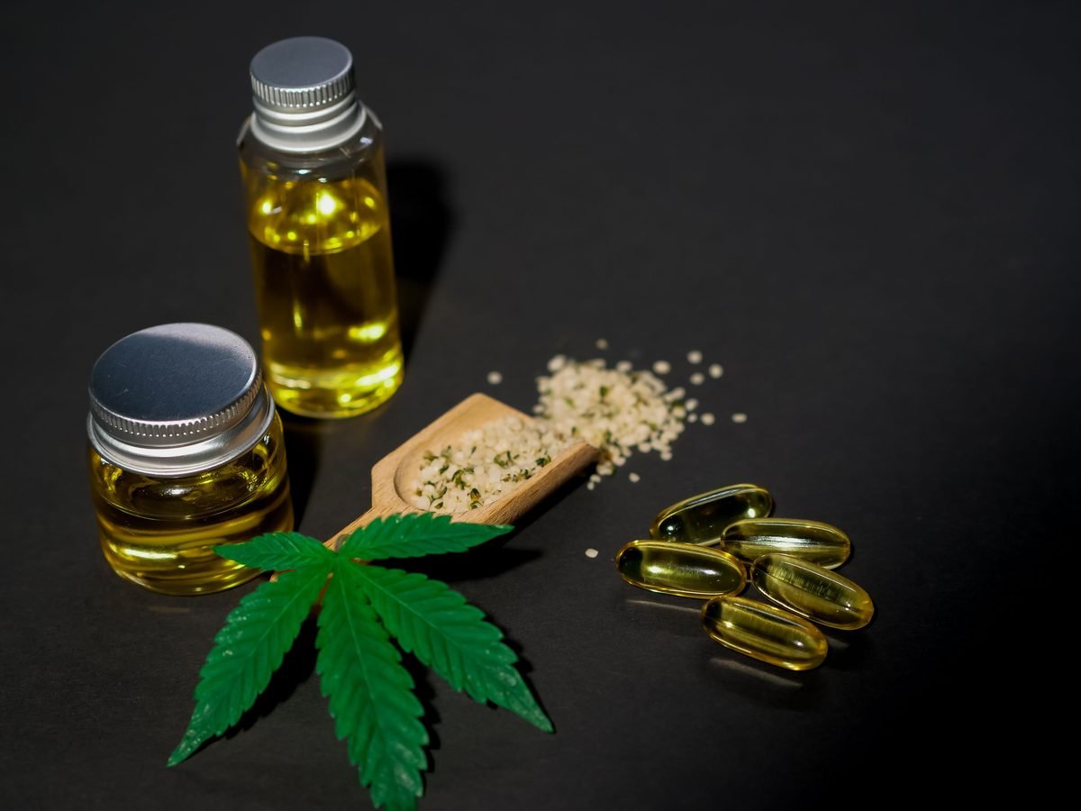 Frascos de óleo, cápsulas e folha de cannabis sobre bancada escura